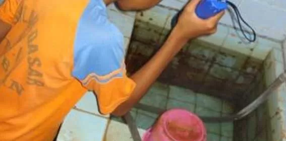 Seorang anak sedang membubuhkan bubuk abate ke dalam bak mandi
