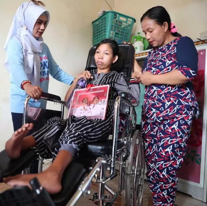 KURSI RODA: Ketua TP-PKK Tanbu Hj Sadariah (kiri) menyerahkan kursi roda baru untuk Lilis yang mengalami disabilitas. (Foto Karyono/Radar Banjarmasin).