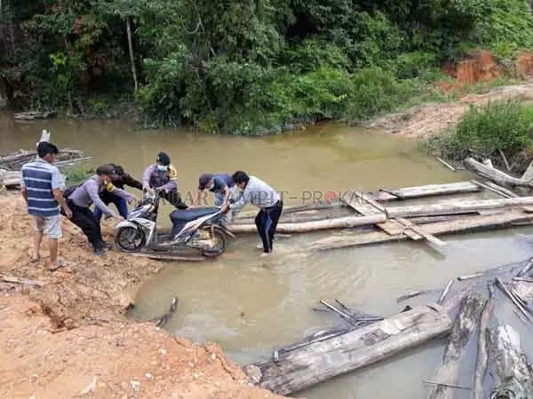 PUTUS: Polsek Marikit hadir membantu masyarakat menyeberangkan sepeda motor, untuk melewati jembatan putus.(HARI/RADAR SAMPIT)