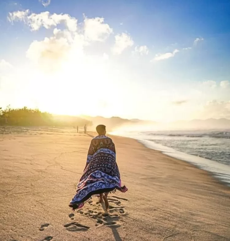 Foto dari belakang biar jejak kakinya kelihatan estetik, pose melihat pantai sambil jalan pake selendang