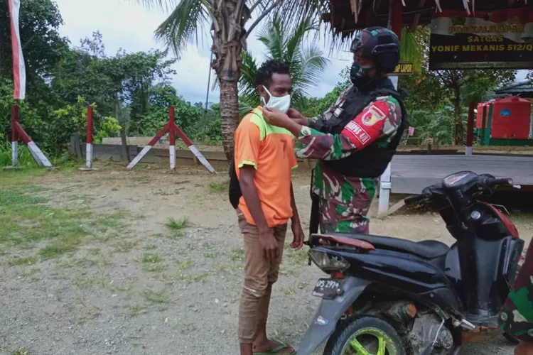 Anggota Satgas Yonif Mekanis 512 QY memasangkan masker kepada warga yang melintas (Satgas Yonif Mekanis 512 QY/Bahman)