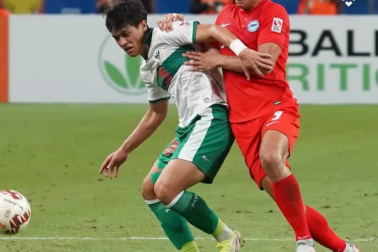 Pemain Indonesia Dewangga (jersey putih hijau) berduel dengan Ikhsan Fandi pemain Singapura (jersey merah) pada pertandingan semifinal leg ke-1 piala AFF Suzuki Cup 2020 ( Instagram/@affsuzukicup )