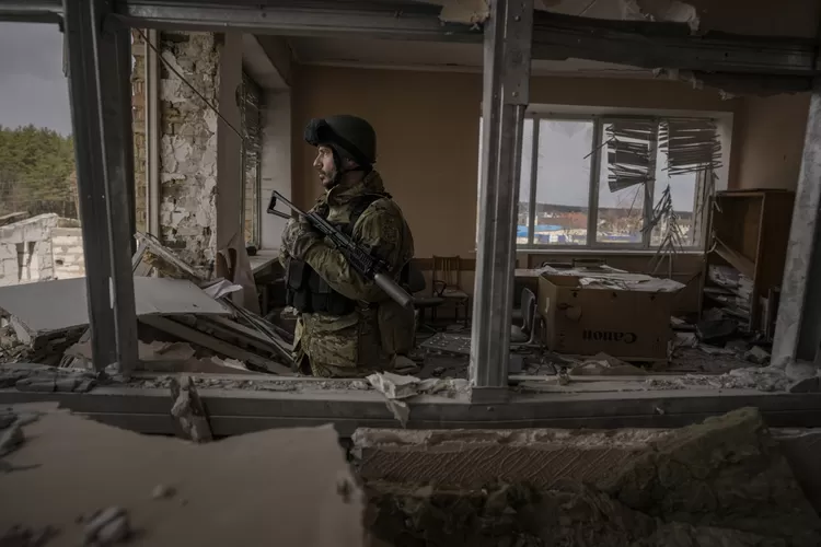Seorang anggota dinas Ukraina berdiri di gedung yang rusak berat di Stoyanka, Ukraina, 27 Maret 2022. (AP Foto)