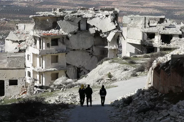 Orang-orang berjalan melewati bangunan yang rusak di Jabal al-Arbaeen yang dikuasai oposisi, di provinsi selatan Idlib, barat laut Suriah, 20 Maret 2022. (REUTERS)
