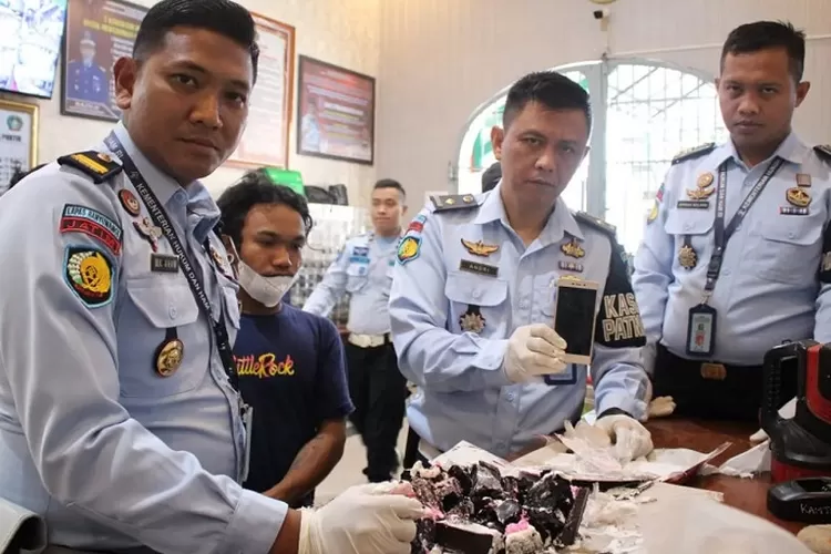 Petugas saat menunjukkan barang bukti handphone dan kue tart (Istimewa)