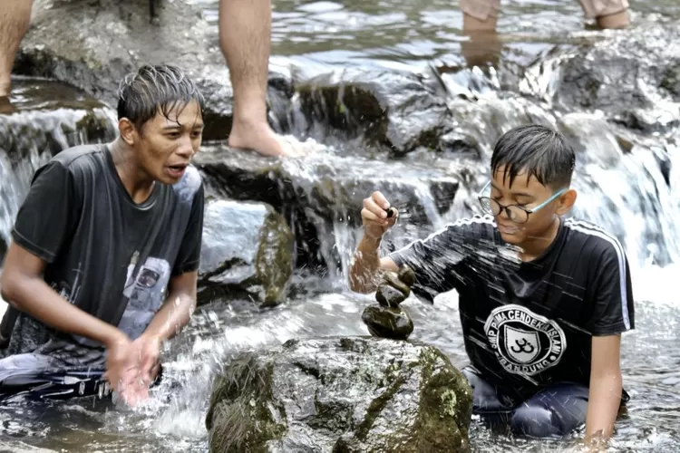 Seorang siswa SMP Pirma Cendekia Islami (PCI)  asik menyusun batu-batuan yang ada daliran sungai sambil diciprati air oleh siswa lainnya - Foto: Henry Lukmanul Hakim