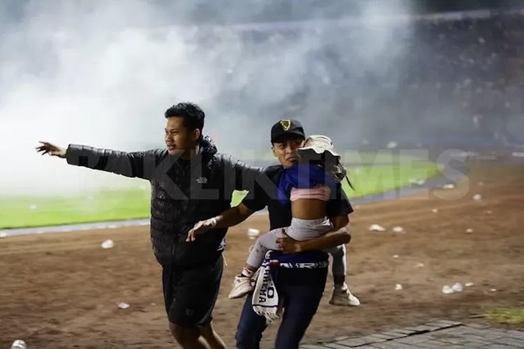 Seorang bapak menyelamatkan diri sambil menggendong putrinya dalam kerusuhan sepakbola yang menjadi tragedi stadion Kanjuruhan Malang di mana 127 orang meninggal dunia. (Twitter @faktasepakbola)