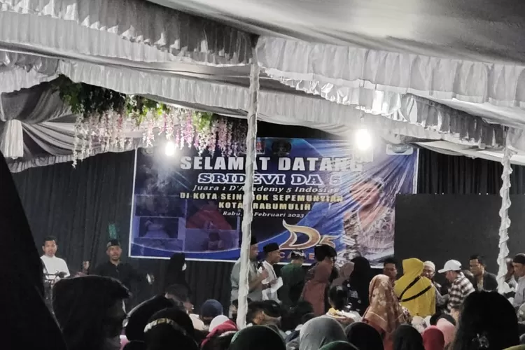 Ibu Sri Devi DA 5 tiba tiba jatuh pingsan di atas panggung. Suasana acara syukuran kemenangan Sri Devi  di ajang DA 5 itu pun  mencekam dan panik.