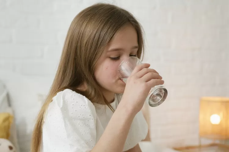 Ilustrasi anak perempuan sedang minum air putih di pagi hari dan manfaat nya (Artem Podrez via Pexels)