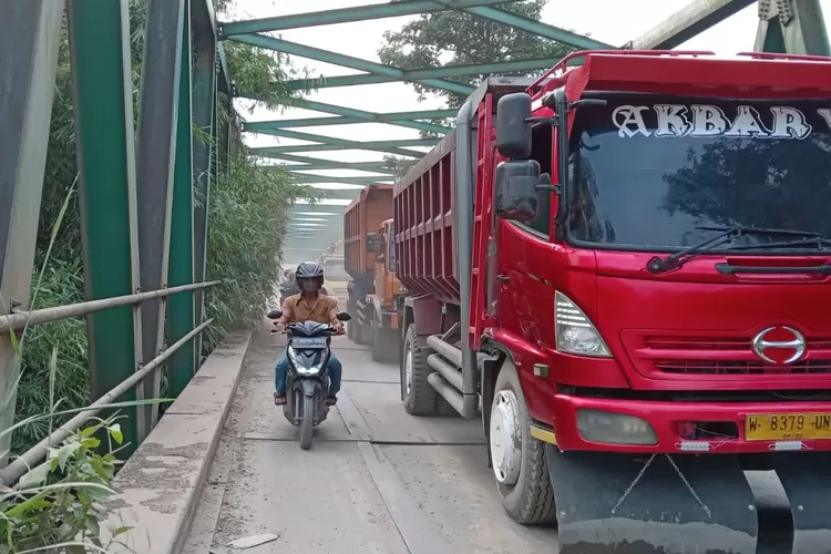 Pengendara motor di antara truk tambang di Jembatan Leuwiranji.