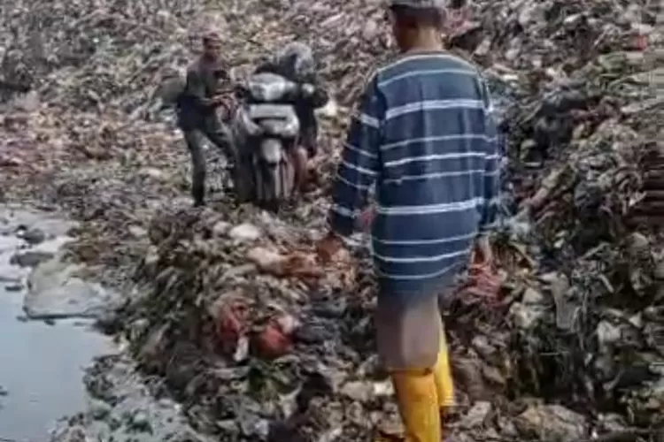 Warga mendorong motor saat melintas akses jalan yang tertutup akibat longsor sampah di TPA Burangkeng, Jumat (9/12/2022). Istimewa. 