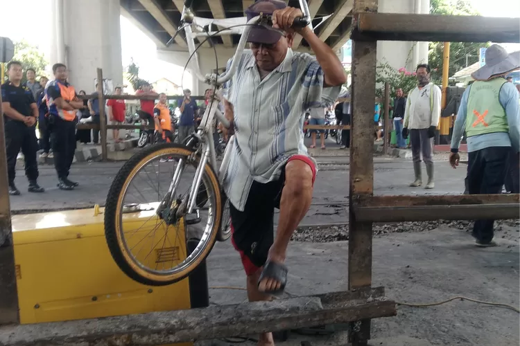 Seorang warga menerobos mengangkat sepeda melalui penutup perlintasan kereta di bawah Jembatan Layang Janti