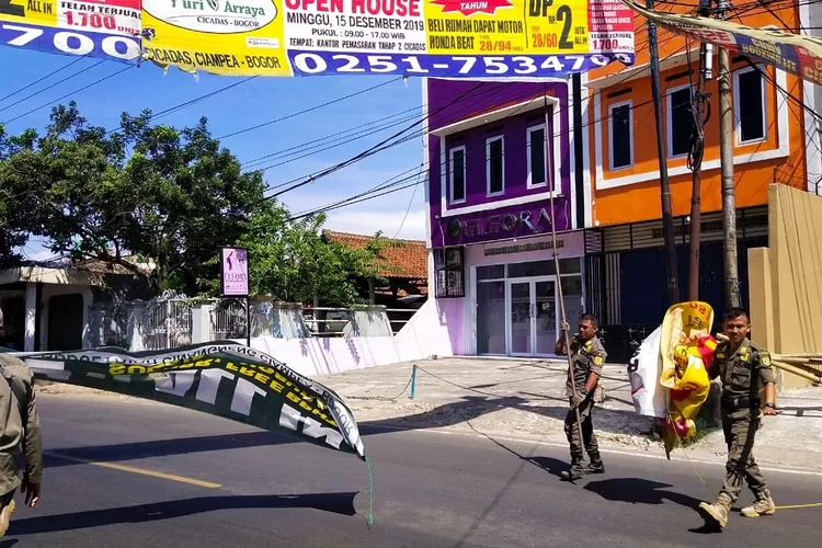 PENERTIBAN: Anggota Pol PP Kecamatan Ciampea menurunk-an spanduk tak berizin, kemarin.
