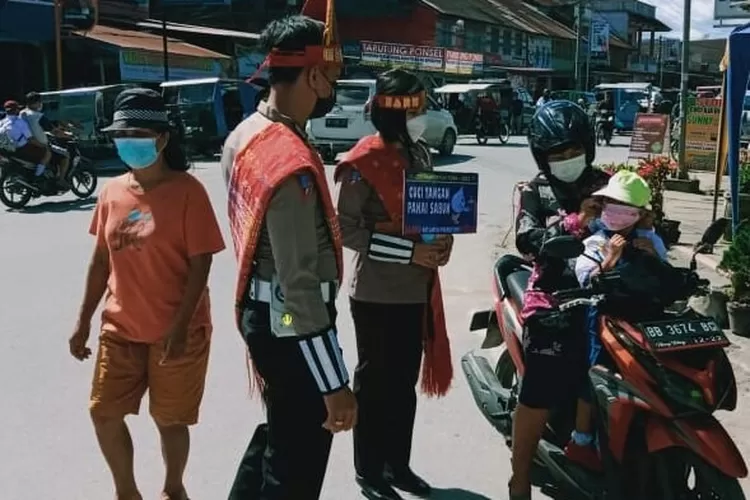 Menggunakan pakaian adat, petugas menyapa pengguna jalan seraya memakaikan masker. (foto Ist)