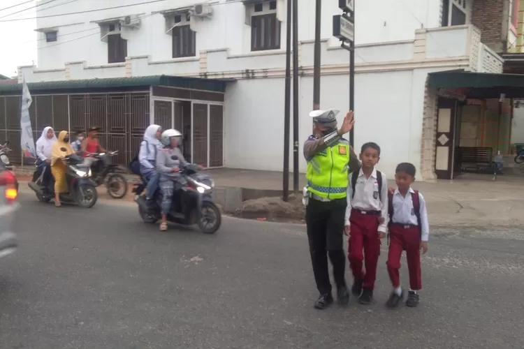 Personil Satlantas Polres Batubara bantu anak sekolah menyeberangi jalan. (Photo:Realitasonline/H.Guntur Sinaga).